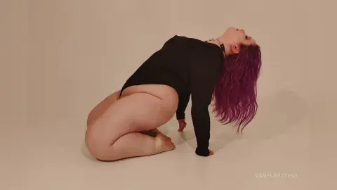 Curvy woman with purple hair in a black bodysuit posing gracefully against a neutral studio background.