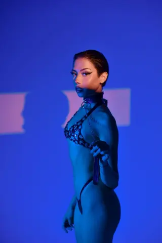 Glamorous woman in black sequin lingerie posing under moody blue studio lighting.