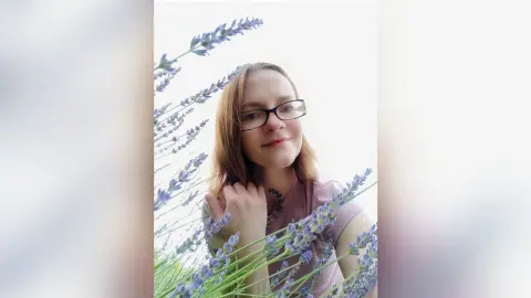 Smiling woman with glasses in a pink top relaxing in a dreamy lavender field.