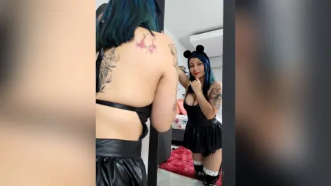 Tattooed woman in a black cosplay outfit with bear ears posing in a bedroom mirror.