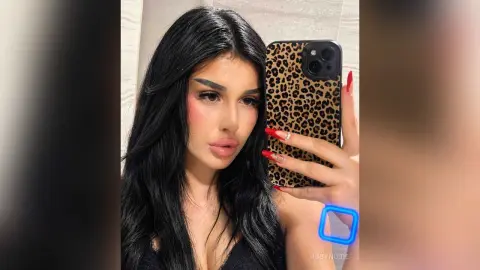 Young woman with long dark hair and pink blush taking a mirror selfie in a stylish leopard print phone case.