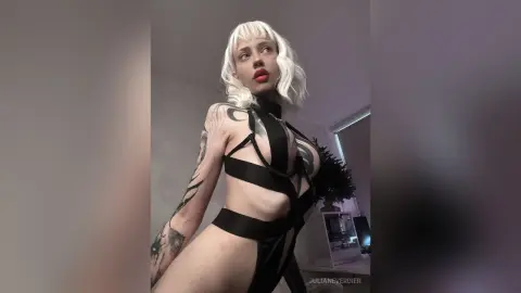 Blonde woman in a black strappy cutout bodysuit posing with a confident mood in a modern indoor setting.