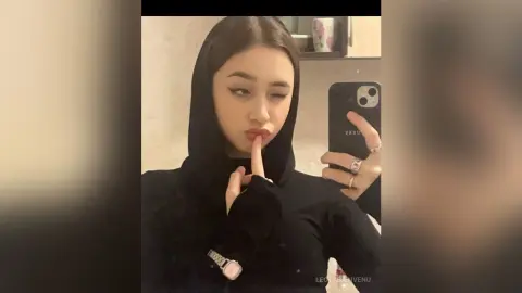 Young woman in a black hijab taking a playful selfie in a modern indoor setting.