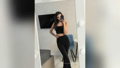 CatherineThomase — CatherineThomase poses for a mirror selfie wearing a black crop top and tight black pants.