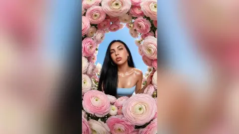 Beautiful woman in a blue top posing within a dreamy pink flower frame against a soft blue sky background.