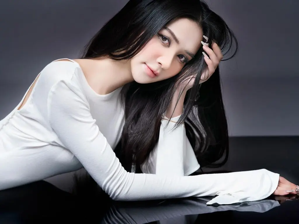 Elegant woman in a white long-sleeve top posing gracefully against a dark studio background.