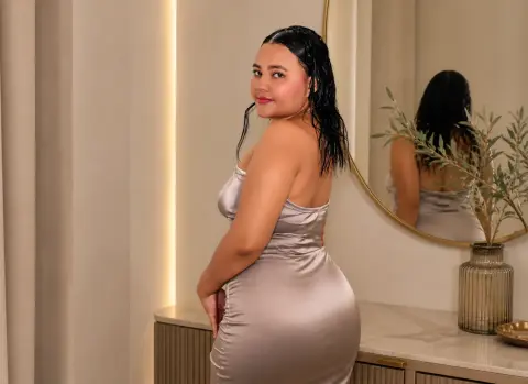 Woman in a silver satin slip dress posing in a modern, elegant bedroom setting.
