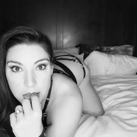 Beautiful woman in black lingerie relaxing on a white bed in a moody black and white portrait.