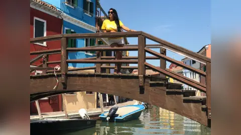 MissyJolie stands on a wooden bridge overlooking a canal, wearing a yellow t-shirt and white shorts with sunglasses.