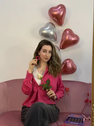 Young woman in a pink button-down shirt holding a rose near heart balloons for a romantic Valentine's Day mood.