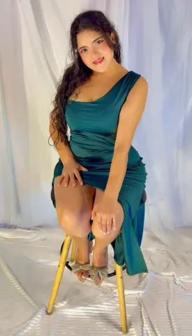 Young woman in an elegant emerald green satin dress sitting against a white backdrop for a glamorous portrait.