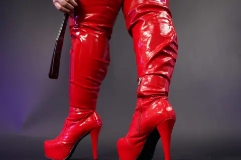 Woman wearing shiny red patent leather thigh-high stiletto boots in a studio setting.