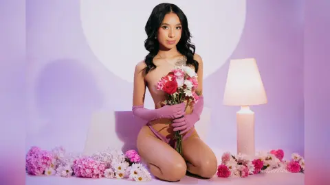Young woman in pink gloves holding red roses in a soft purple studio setting with dreamy lighting.