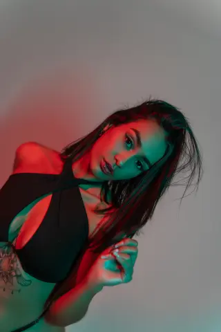 Young woman in a black halter top posing under moody red and teal studio lighting.
