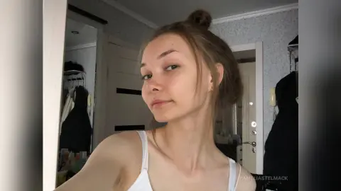 Young woman in a white tank top with a messy bun posing in a bright indoor room.