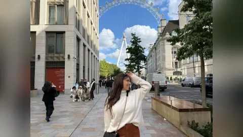 Smiling woman in a white sweater standing on a London street near the London Eye on a sunny day.