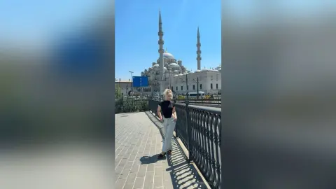 Blonde woman in black top and light trousers standing by a railing near the Blue Mosque in Istanbul.
