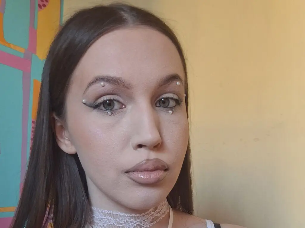 Young woman with winged eyeliner and facial gems posing against a colorful wall in a soft, natural light mood.