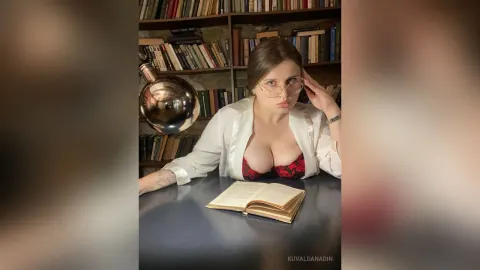 KuvaldaNadin — KuvaldaNadin wears glasses and an open white shirt over a red lace bra while sitting at a desk with an open book.