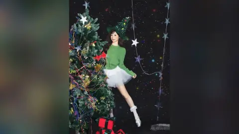 Cheerful woman in a green sweater and white skirt posing by a decorated Christmas tree in a festive setting.