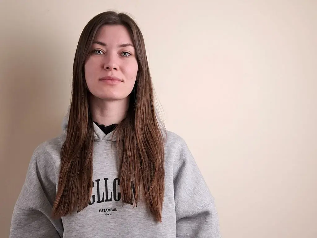 Young woman with long brown hair wearing a grey Istanbul graphic hoodie against a neutral beige wall.