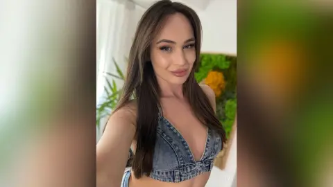 Young woman in a denim crop top posing in a bright, modern room with indoor plants.