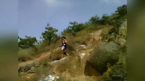 Active woman in black athletic wear hiking up a rocky mountain trail under a clear sky.