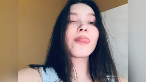 Playful young woman with long dark hair winking and sticking out her tongue in a casual indoor setting.