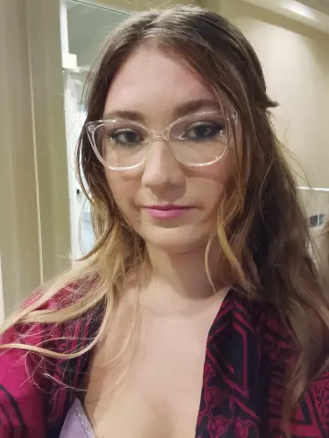 jenellehayesxoxo poses with long blonde hair and clear glasses, wearing a red and black patterned robe.
