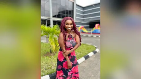 Smiling woman in a floral maxi dress posing outdoors near palm trees in front of a modern building.