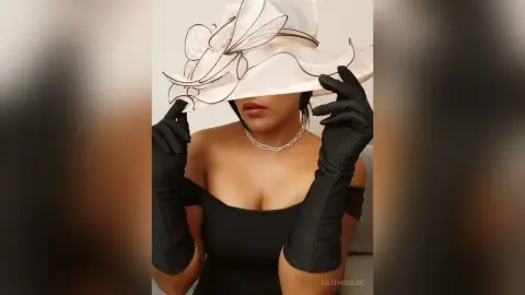 Elegant woman in a black off-the-shoulder dress and long gloves wearing a large white wide-brimmed sun hat.