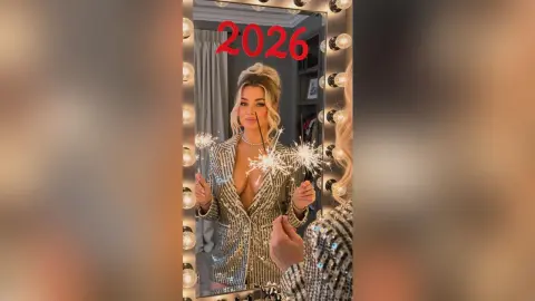 Glamorous woman in a silver sequin blazer posing with sparklers in a lighted vanity mirror for New Year's Eve.