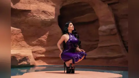 Elegant woman in a purple satin dress posing confidently by a desert rock formation and pool.