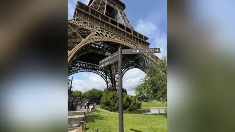 Low angle view of the Eiffel Tower in Paris under a blue sky with a street sign in the foreground.
