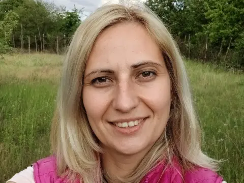 Smiling blonde woman in a pink vest relaxing in a lush green summer meadow.