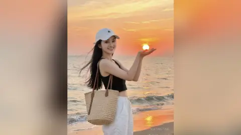 Smiling woman in a black tank top and white cap holding the sunset sun at a peaceful beach.