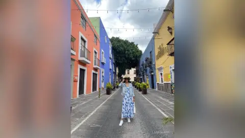 Stylish woman in a blue floral dress walking down a colorful cobblestone street in a vibrant historic town.