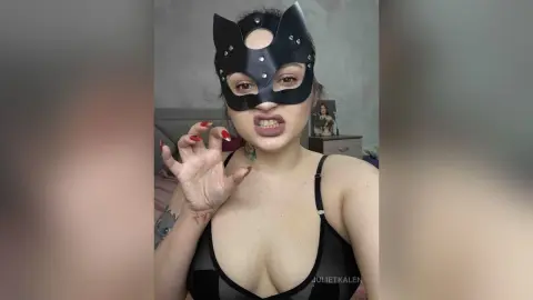 Woman in black cat mask and lingerie posing playfully in a bedroom setting.