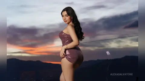 Elegant woman in a sparkling pink mini dress posing against a dramatic sunset sky over mountain silhouettes.