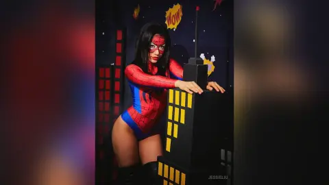 JessieLiu wears a red and blue Spider-Man bodysuit while posing behind a black building prop.