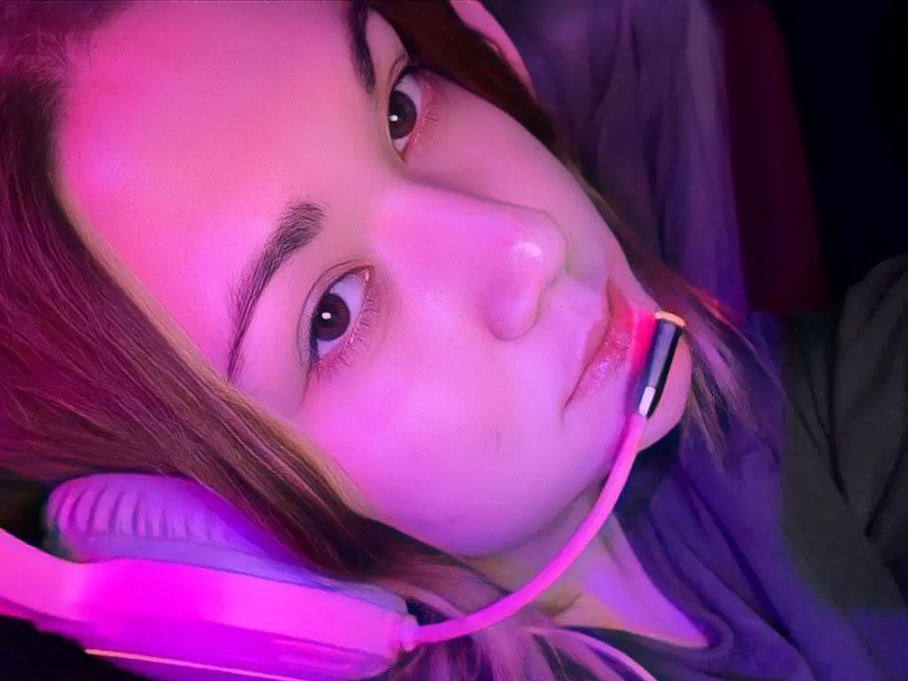 Close-up portrait of a young woman wearing pink headphones in moody neon pink lighting.