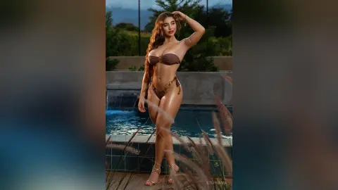 Glamorous woman in a brown bikini posing by a luxury swimming pool at dusk.