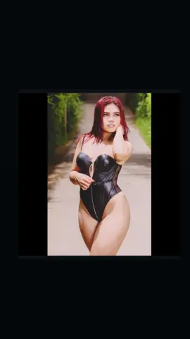 Red-haired woman in a black lace bodysuit posing on a sunny outdoor path with a soft, romantic mood.