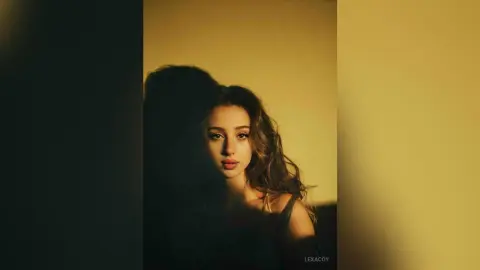 Moody portrait of a young woman with long wavy hair in warm, cinematic lighting.