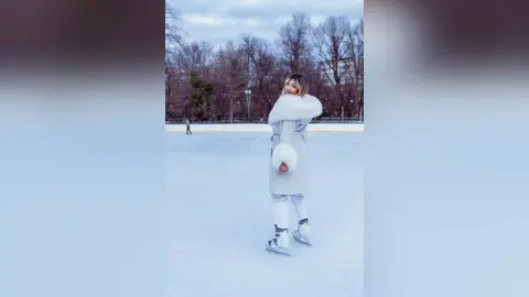 Young woman in a white winter coat and ice skates enjoying a serene day at an outdoor frozen ice rink.