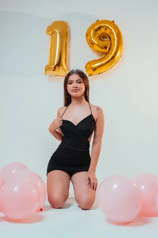 Young woman in a black mini dress celebrating her 19th birthday with gold and pink balloons.