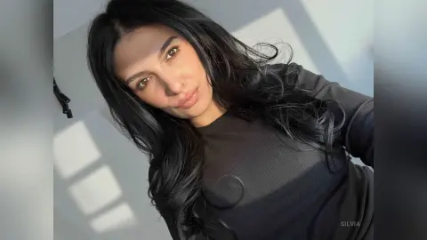 Smiling woman with long dark hair wearing a black ribbed top in bright natural sunlight.