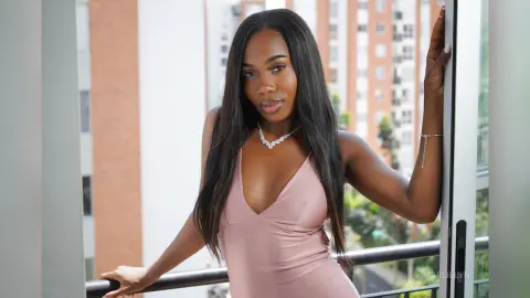 Beautiful Black woman in a pink satin dress posing on a city balcony during a sunny day.