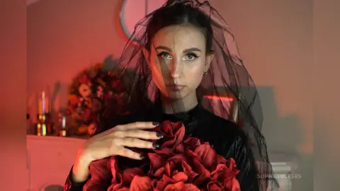 Moody portrait of a woman in a black outfit and veil holding a bouquet of dark red flowers.