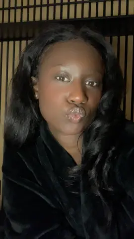 GabriellaGoldx pouts her lips while wearing a black velvet robe against a dark slatted background.